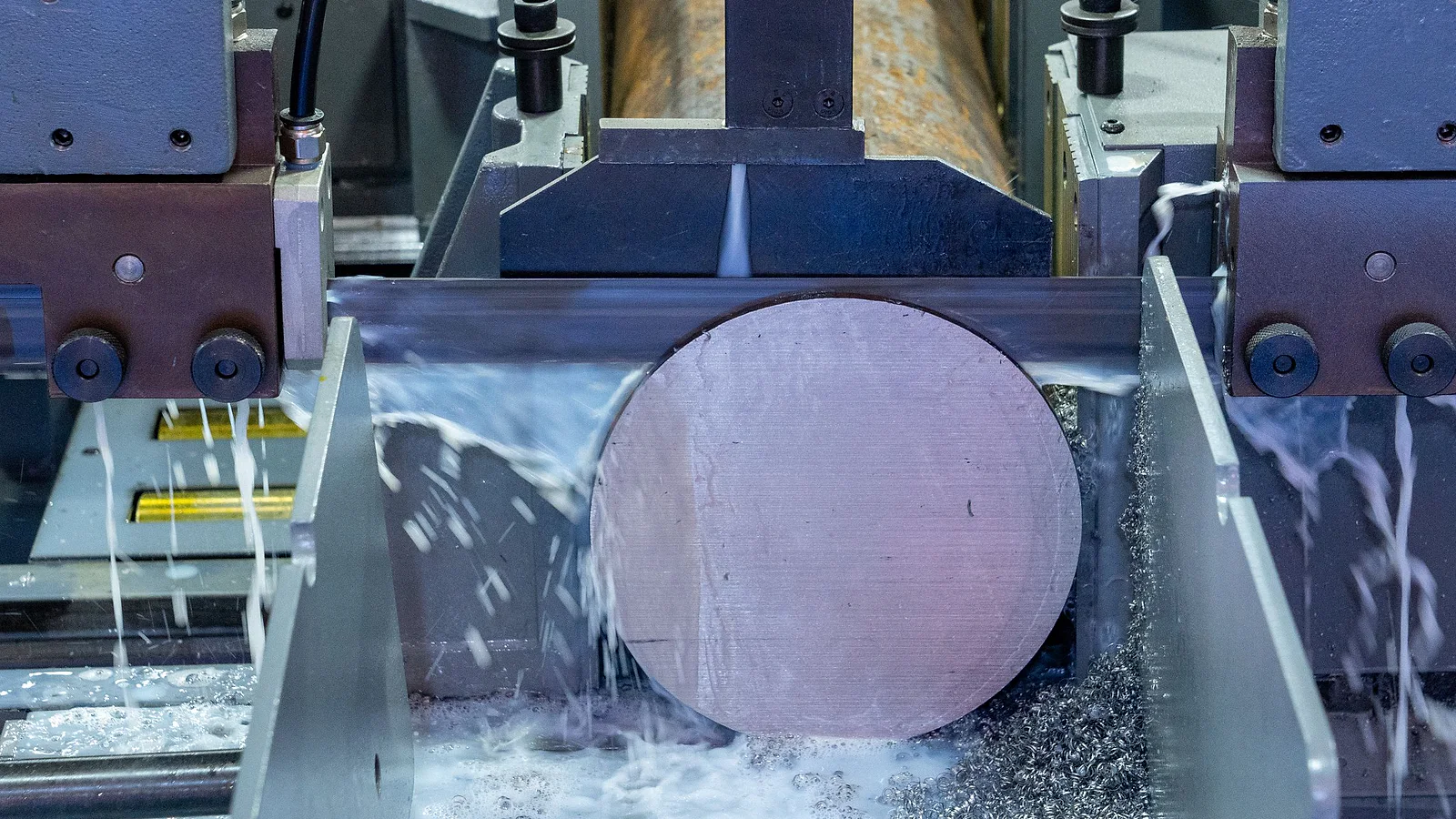 Large solid round bar positioned in an industrial band saw during a production cut