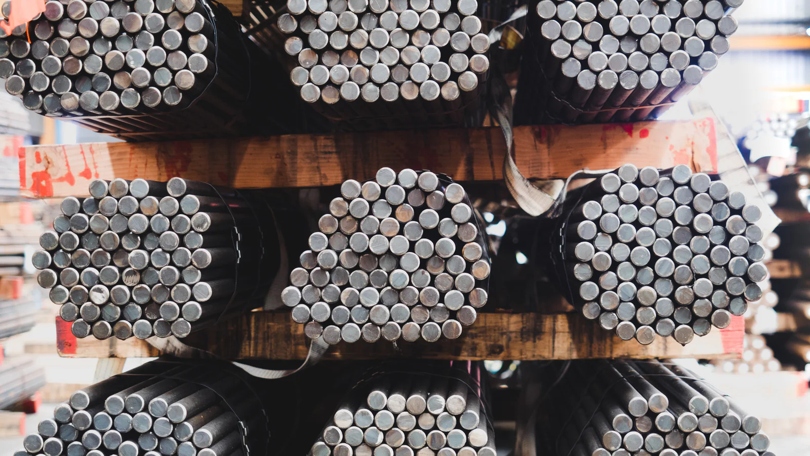 Multiple bundles of solid round steel bar stacked on wood supports