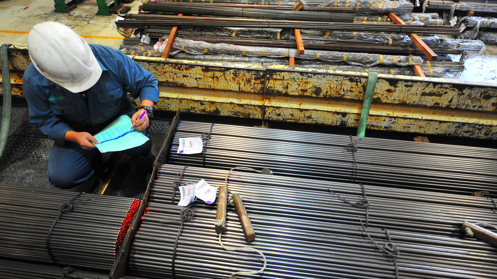 Industrial worker checking documentation beside bundled round steel bars